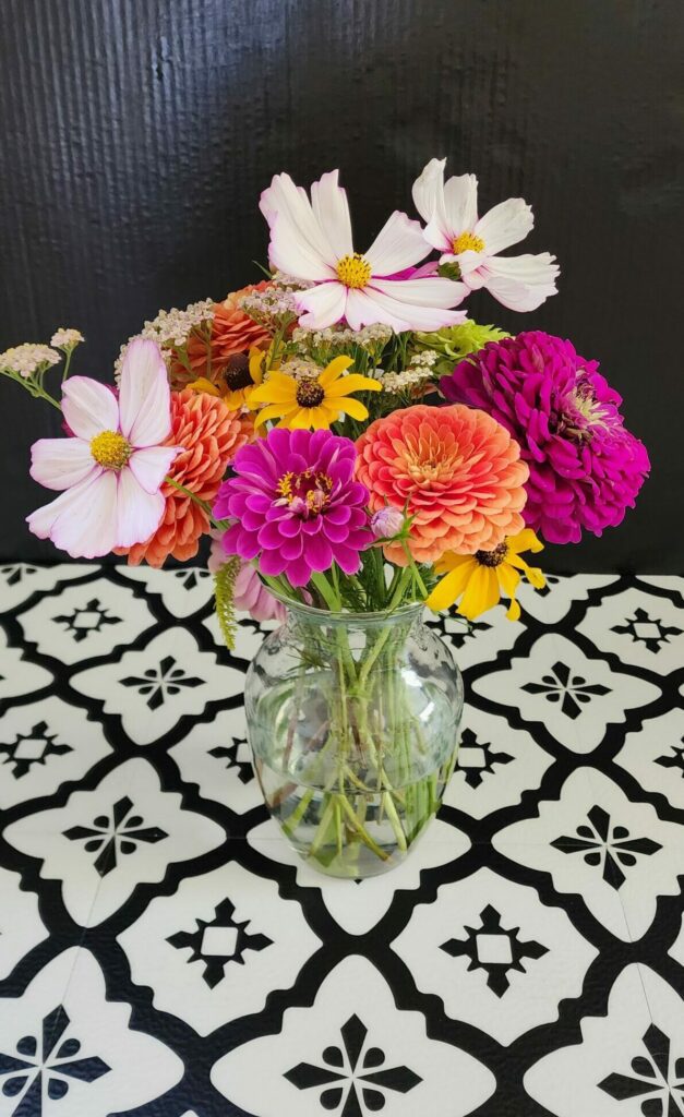 pink, yellow, orange and white flowers sit in a vase on a black and white surface