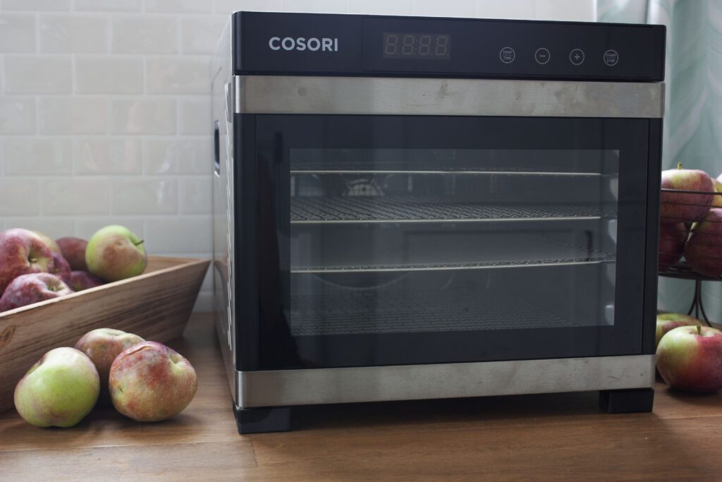 a Cosori metal dehydrator sits on a wood table beside apples