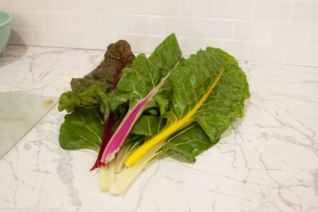 pink, red, yellow and white swiss chard leaves lay on a white counter with white tile backsplash