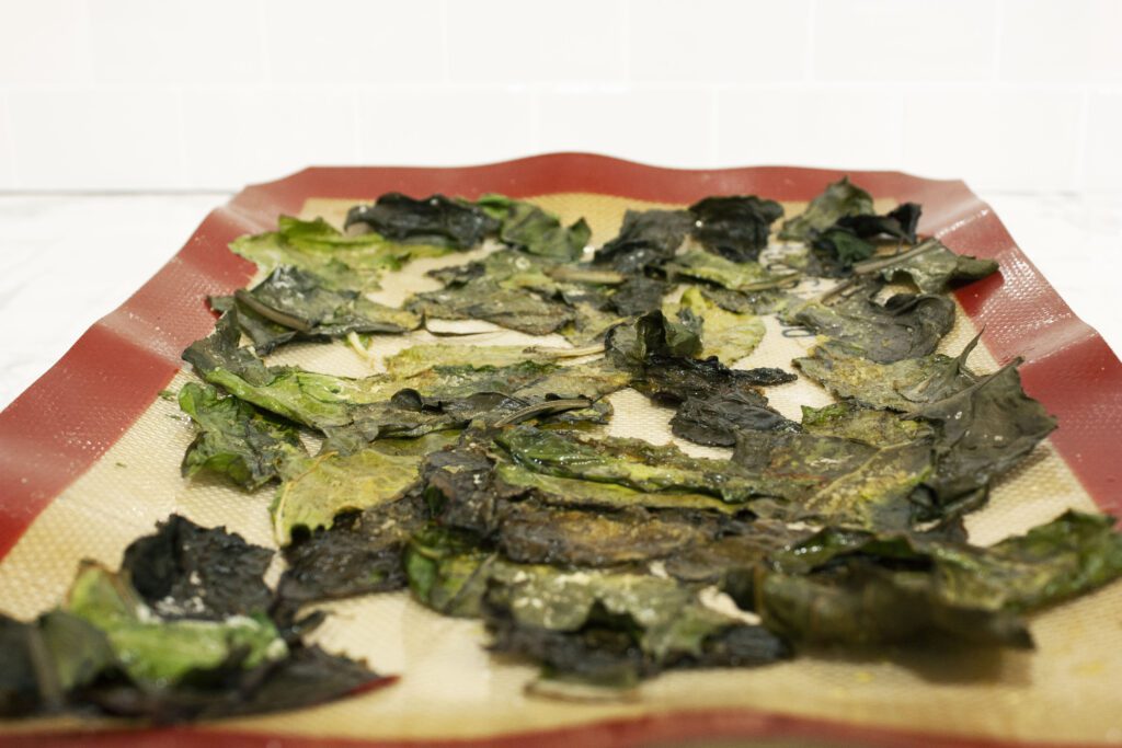a baking sheet is covered in brown, black cooked swiss chard leaves making them into swiss chard chips