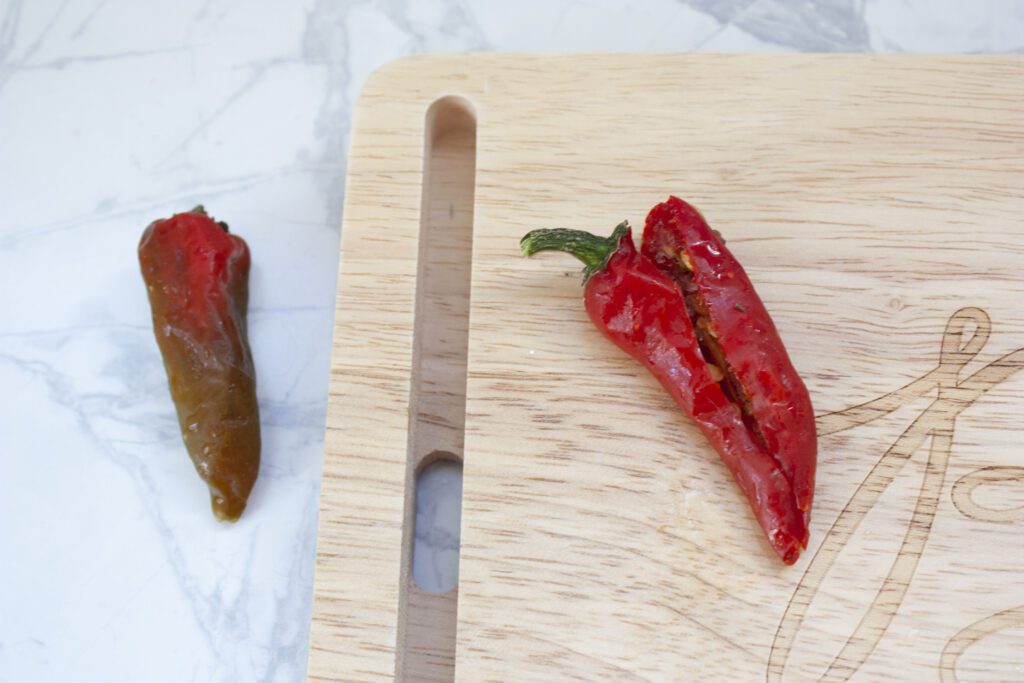 a red hot pepper is cut in half on a wood cutting board with a second red hot pepper sitting on the white counter beside it