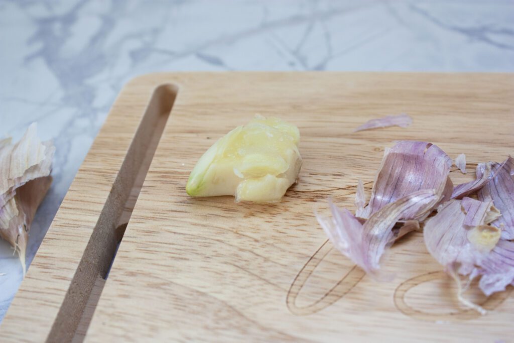 a clove of garlic is peeled and crushed on a wood cutting board