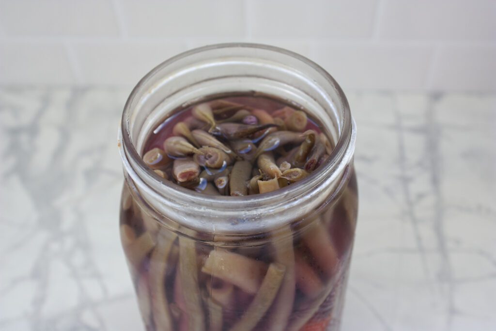 beans are sitting in a pickling brine in an open glass mason jar