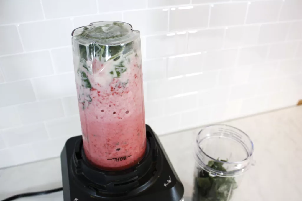 a blender with a single serving smoothie sits on top filled with pink liquid and kale ready to be blended