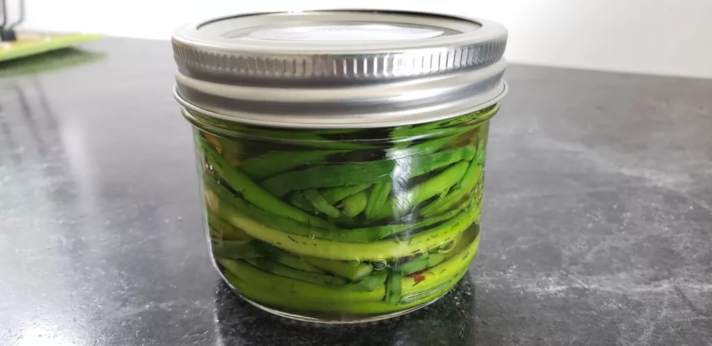 a small jar is filled with pickled garlic scapes