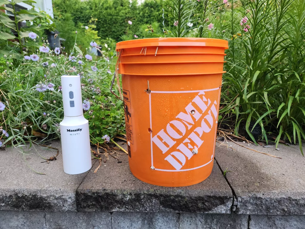 an orange bucket filled with mushroom spawn beside an automatic mister