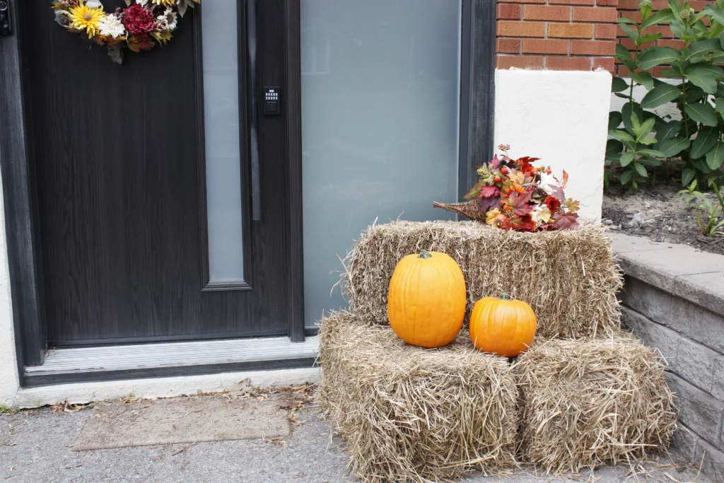 a front porch with 3 straw bales and 2 pumpkins which are used as decorations for fall. A decorative wreath and cornucopia also sit on the front porch
