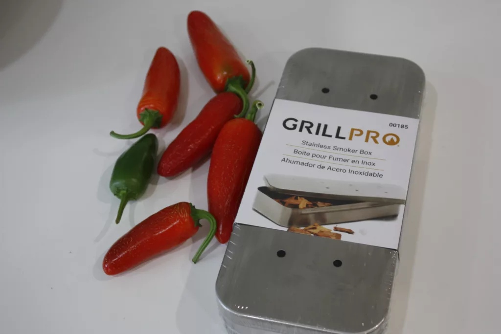 6 jalapeno peppers sit beside a stainless steel smoker box to smoke peppers into chipotle