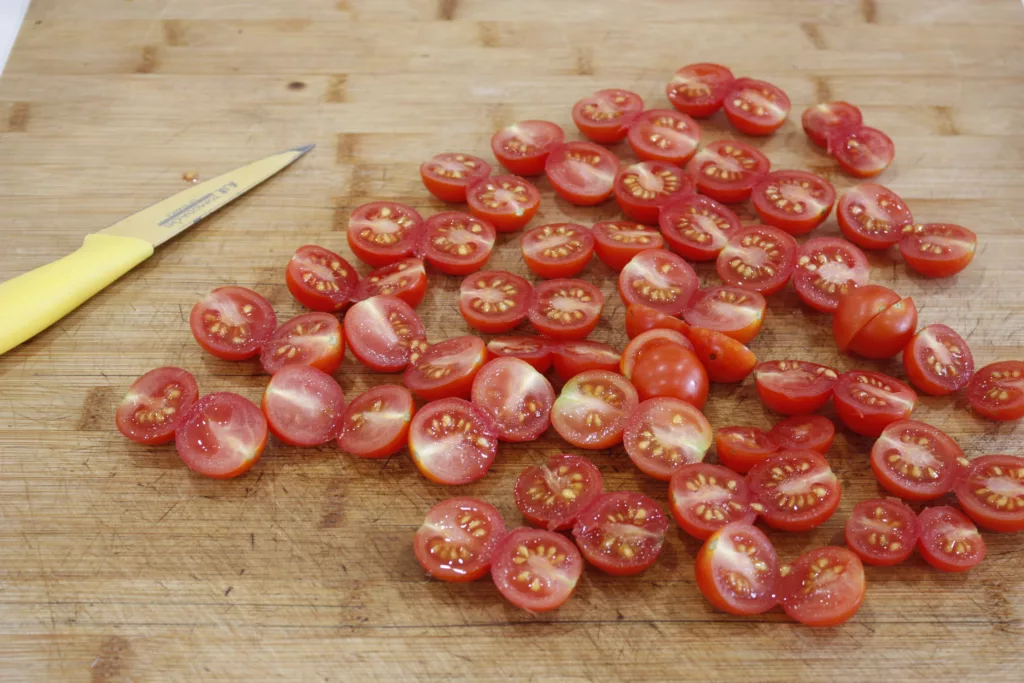 a cutting board is filled with cherry tomatoes cut in half